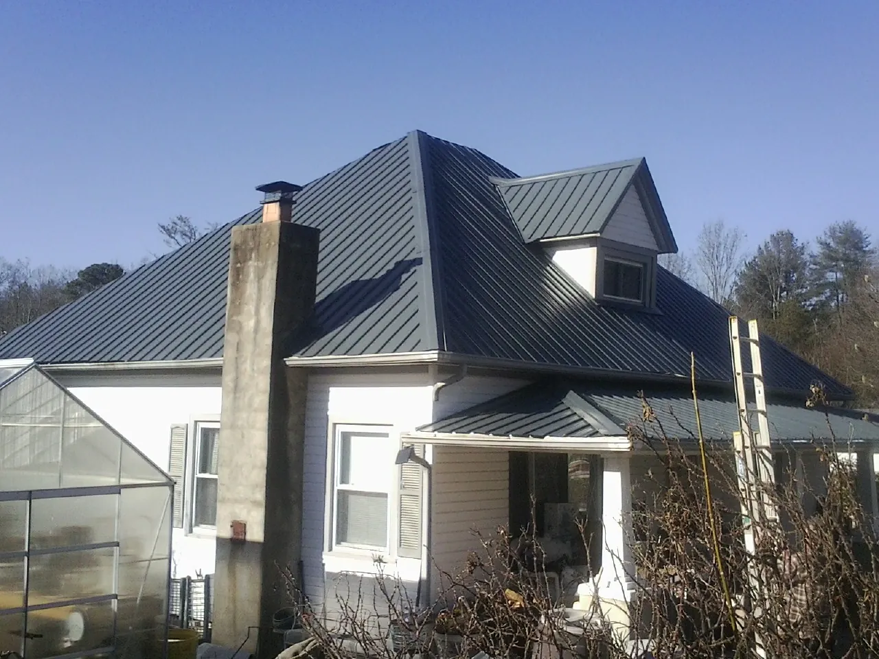 Dark blue standing seam metal roof on a white farmhouse with dormer — Slate & Tile Roof Repair by Roofing Brothers in Knightdale