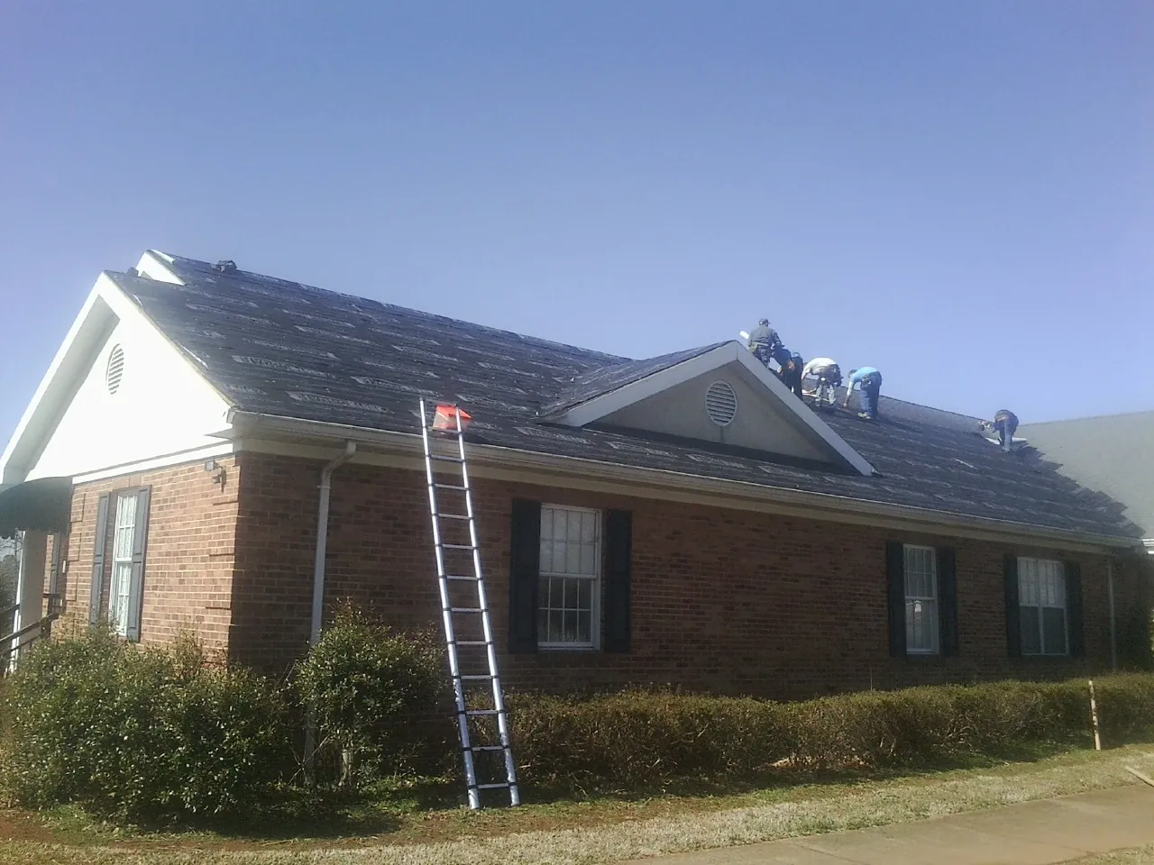 Crew tearing shingles off a brick ranch roof with a ladder set — Emergency Roof Repair work by our crew in Knightdale