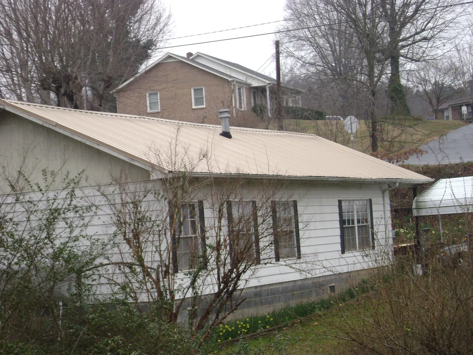 Tan metal roof on a white sided house set into a hillside — Commercial Roofing by Roofing Brothers in Knightdale